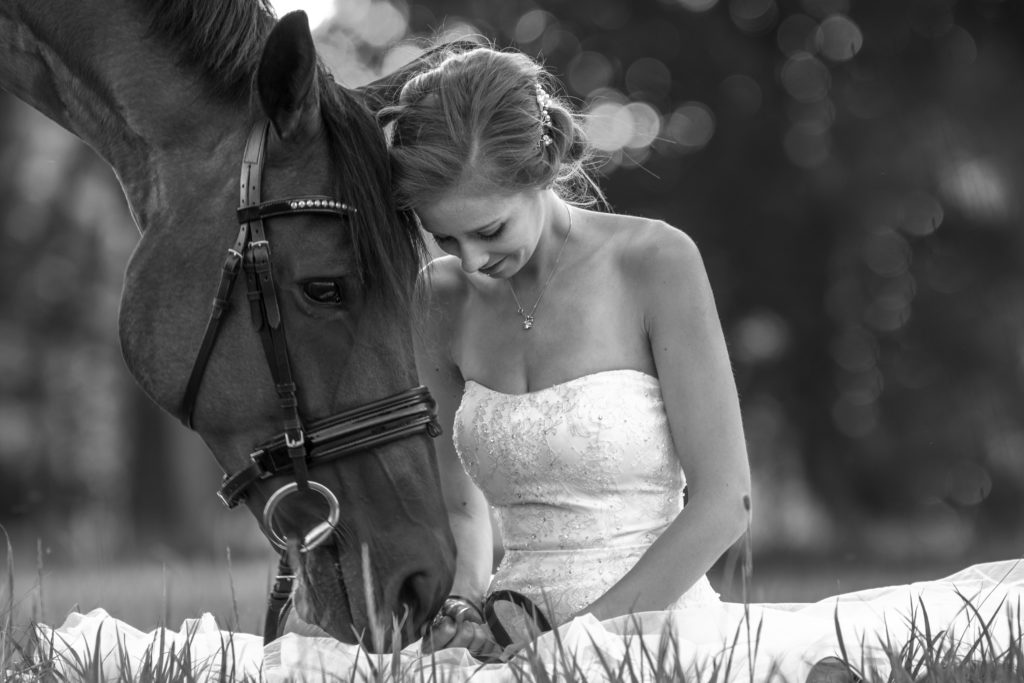 Braut auf Wiese mit Pferd im Hochzeitskleid